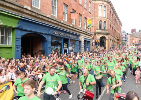 Large group of colleagues in green t-shirts taking part in Pride parade